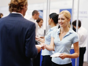 Sales executive giving brochures to businessman at exhibition