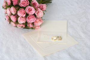 Wedding bouquet of pink roses and wedding rings on invitation
